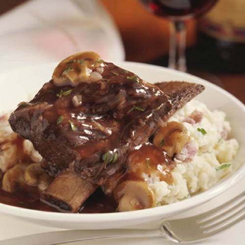 Beef short ribs with mushroom wine sauce on mashed potatoes with red wine glass in background