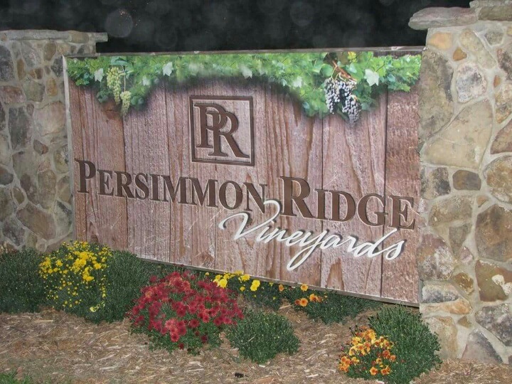 Persimmon Ridge Vineyards Winery LLC - photo of a large sign made of stone and wood that had the winery's logo on it. Some landscaping is in the foreground.