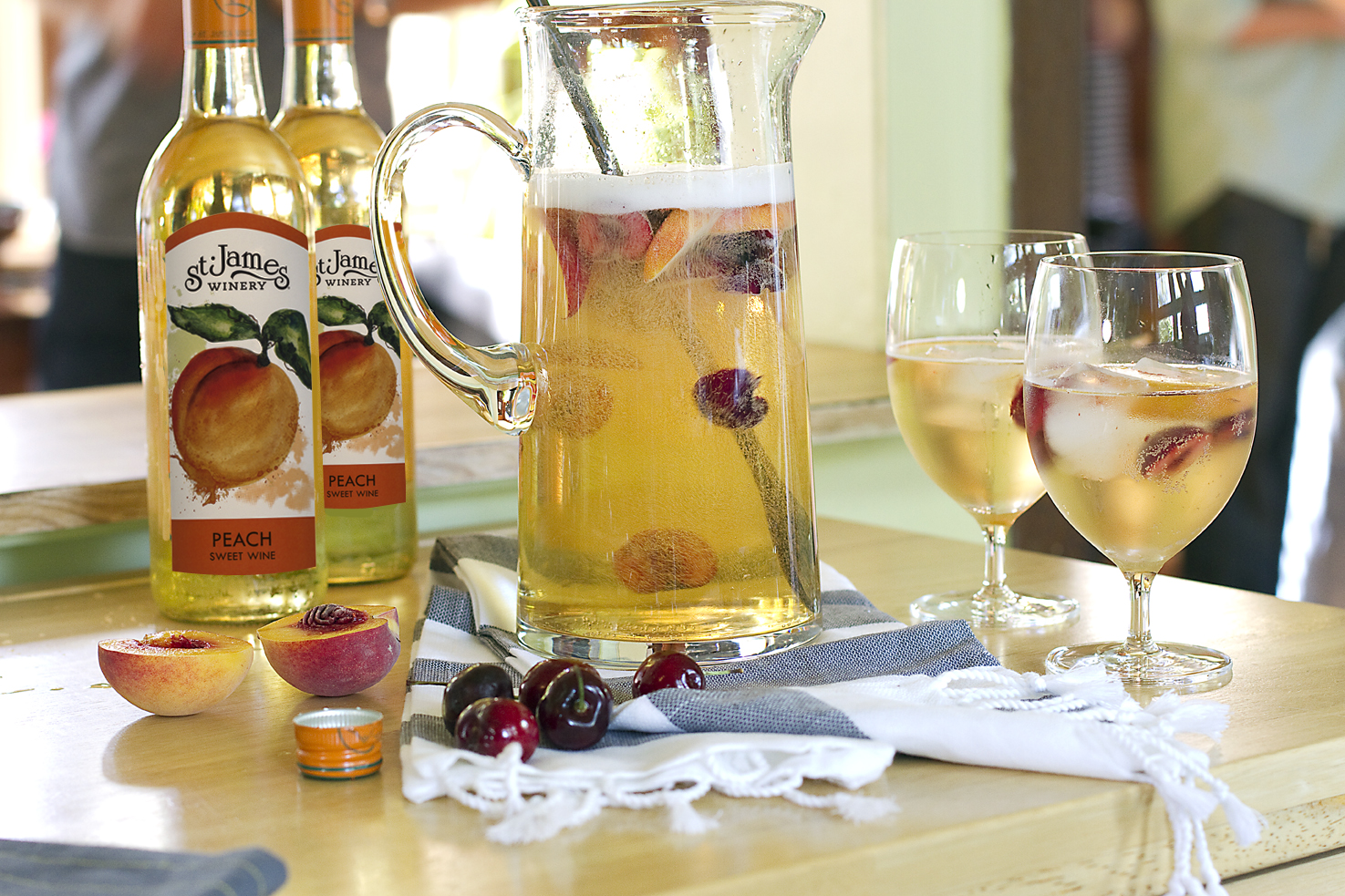 St. James Winery- A jug, two bottles, and two wine glasses filled with peach fruit wine.