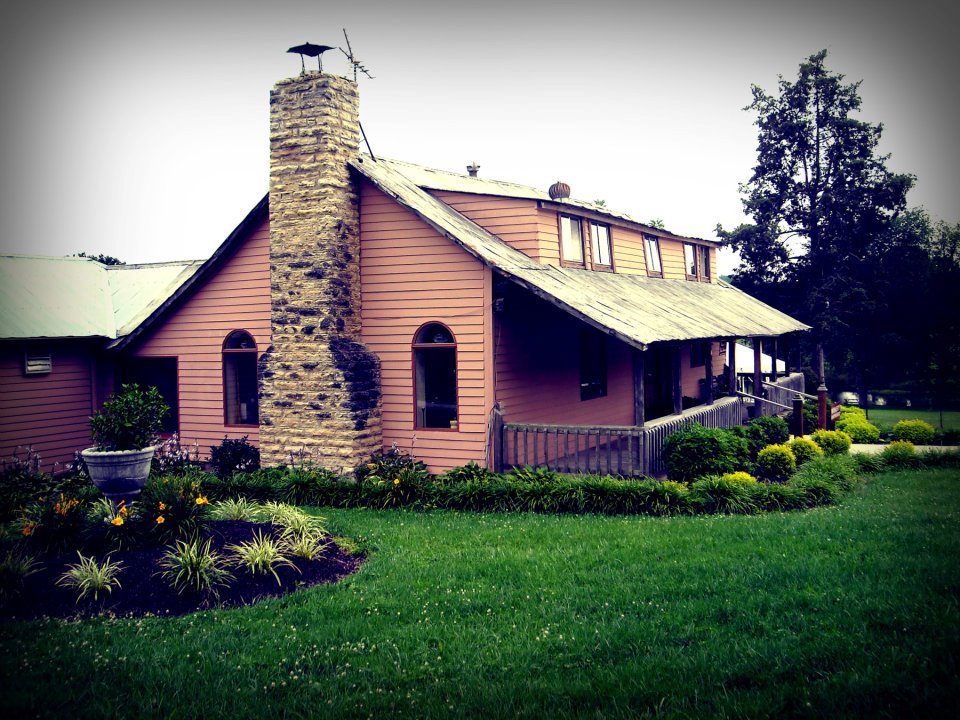 Villa Antonio Winery- A two story brown building with a porch along the front and a stone chimney on the side.