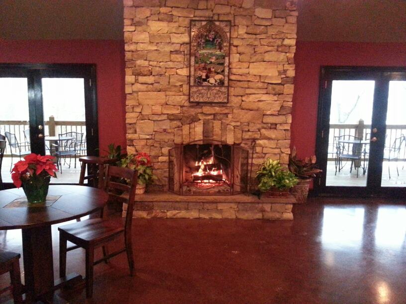 Apple Creek Vineyard & Winery - indoor photo, daytime, of a large brick fireplace in a dining room with windows on either side and a wooden floor with dining furniture.