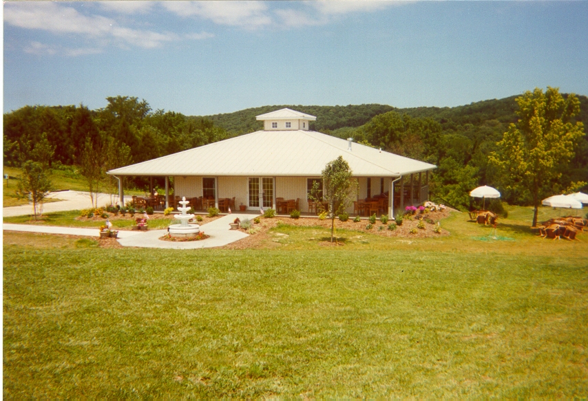 Balducci Vineyards- A white one story building with a fountain, flowers, and trees surrounding it.