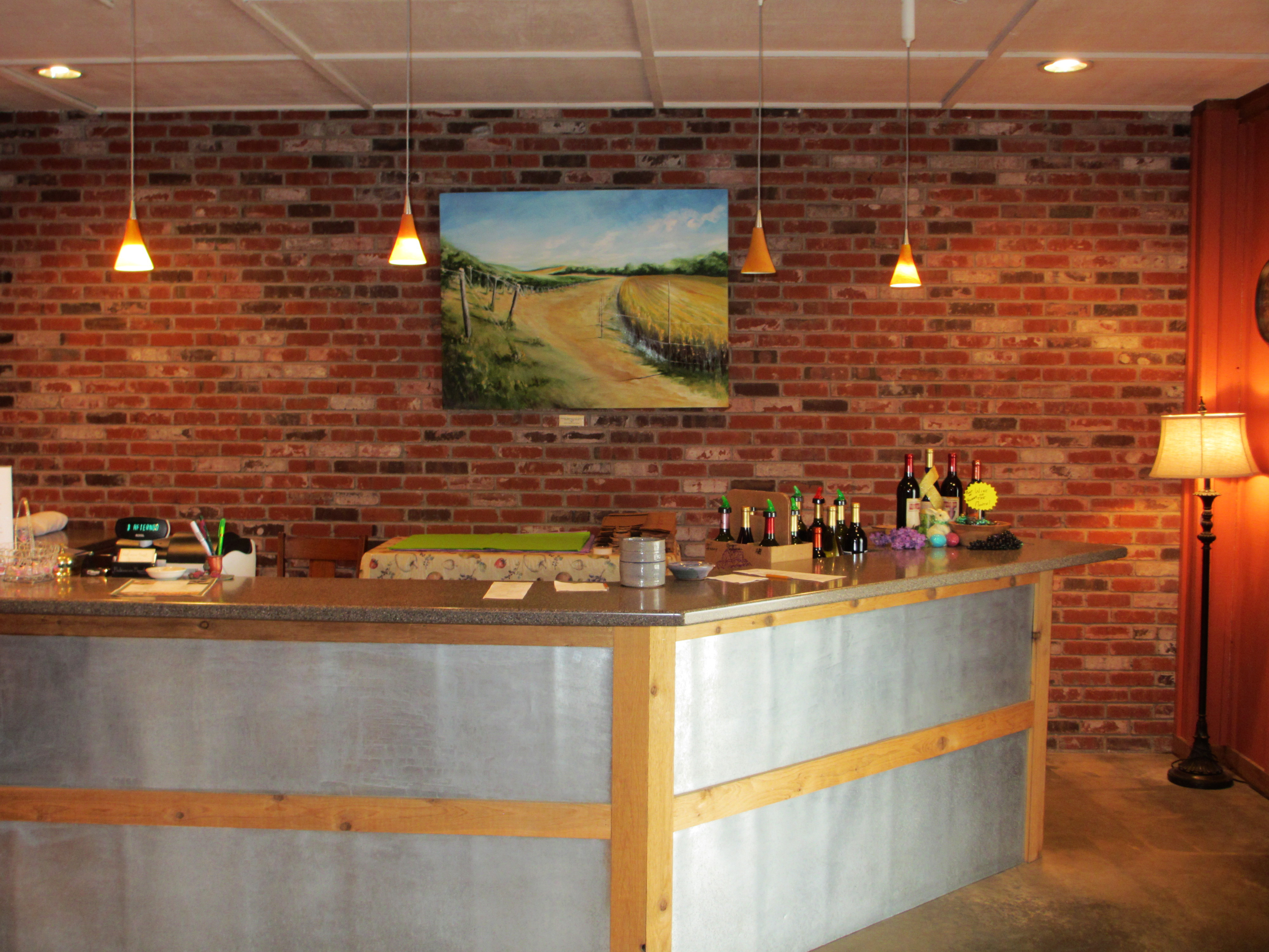 Baltimore Bend Vineyard - interior photo, a bar area constructed of metal and wood in a room with brick walls and overhead lighting.