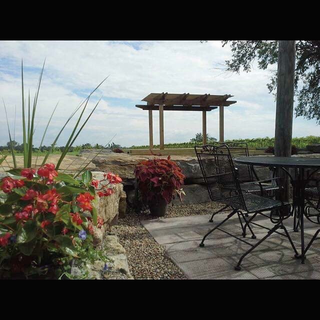 Black Silo Winery - outdoor photo, daytime, of a patio with table and chairs. The patio has a gazebo structure in the background and red flowers and landscaping are visible on the left.