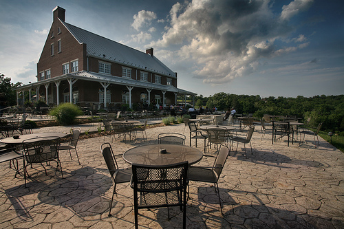 Canterbury Hill Winery and Restaurant - outdoor photo, daytime, of a large patio area with several tables and chairs. There are clouds in the sky, and in the background is a large building.