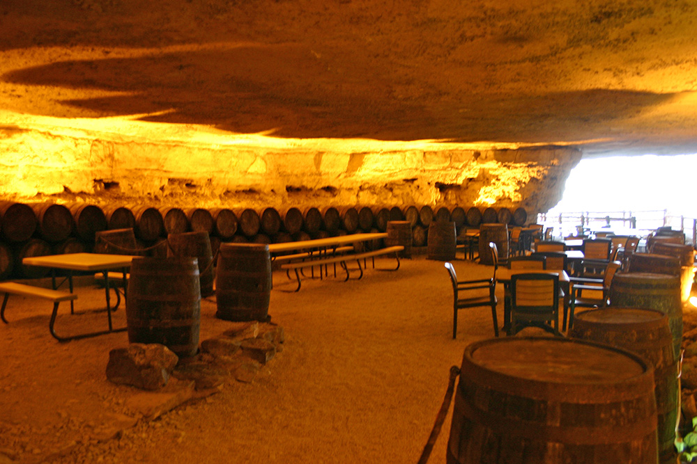Cave Vineyard - indoor photo, daytime, of a large cavernous room with barrels used for aging wine along the far wall, and chairs and tables.