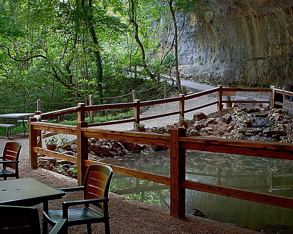Cave Vineyard - outdoor photo, daytime, of a patio area with a table and chairs. There is a path behind the patio which travels near a sheer rock face.