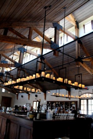 Chandler Hill Vineyards - indoor photo, daytime. It is a large room with high vaulted ceilings and wooden rafters, overhead lighting and a bar.
