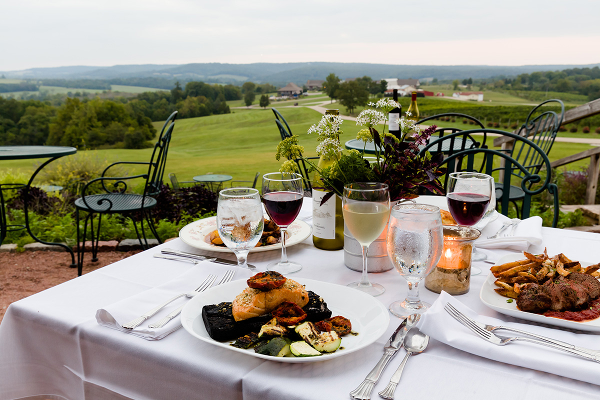 Chaumette Vineyards & Winery - outdoor photo, daytime. A table with meals and place settings is in the foreground. Rolling hills and skies are in the background.