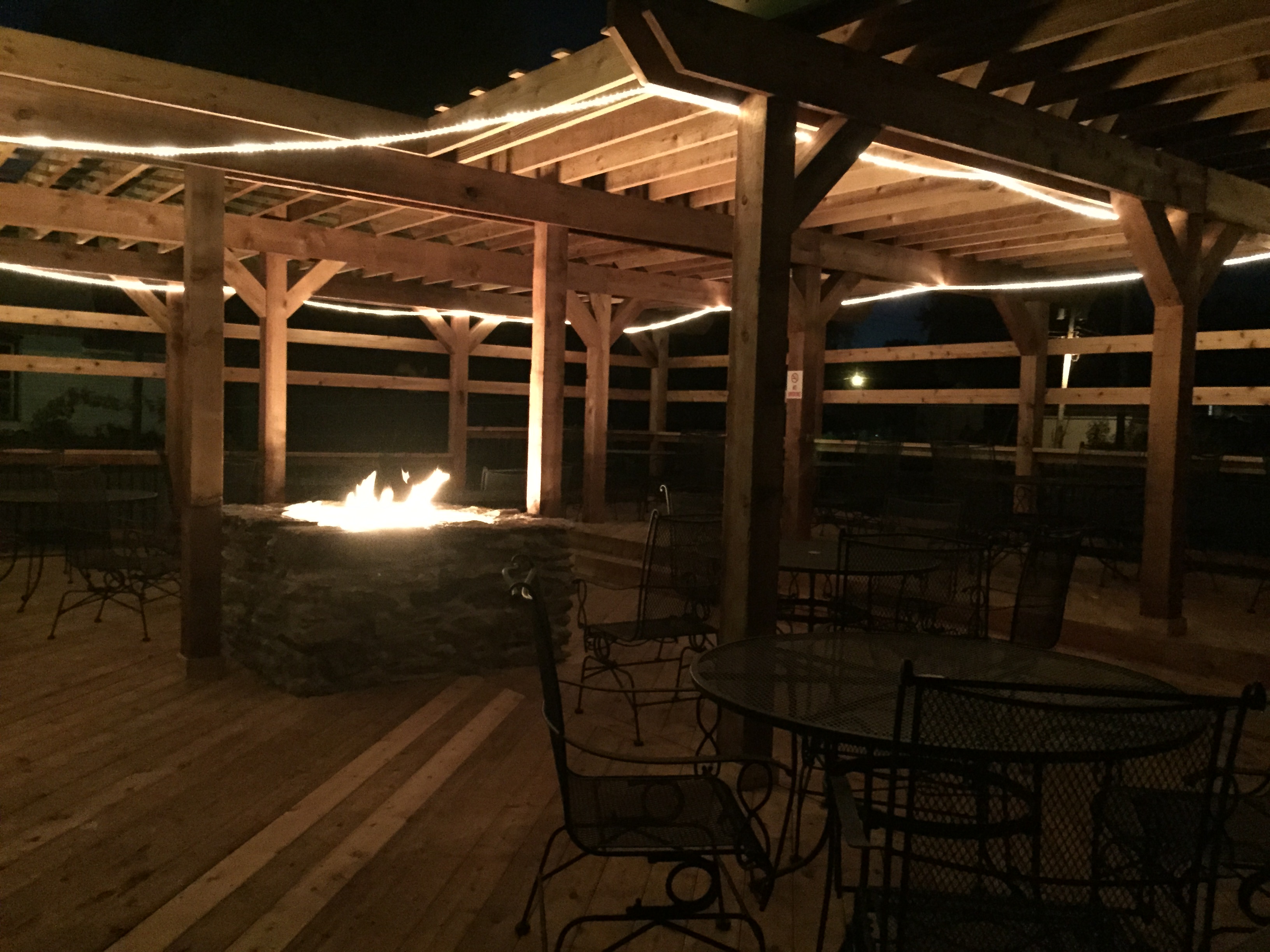 Grindstone Valley Winery - outdoor photo, nighttime. A wooden patio with a lit fire pit in the center.