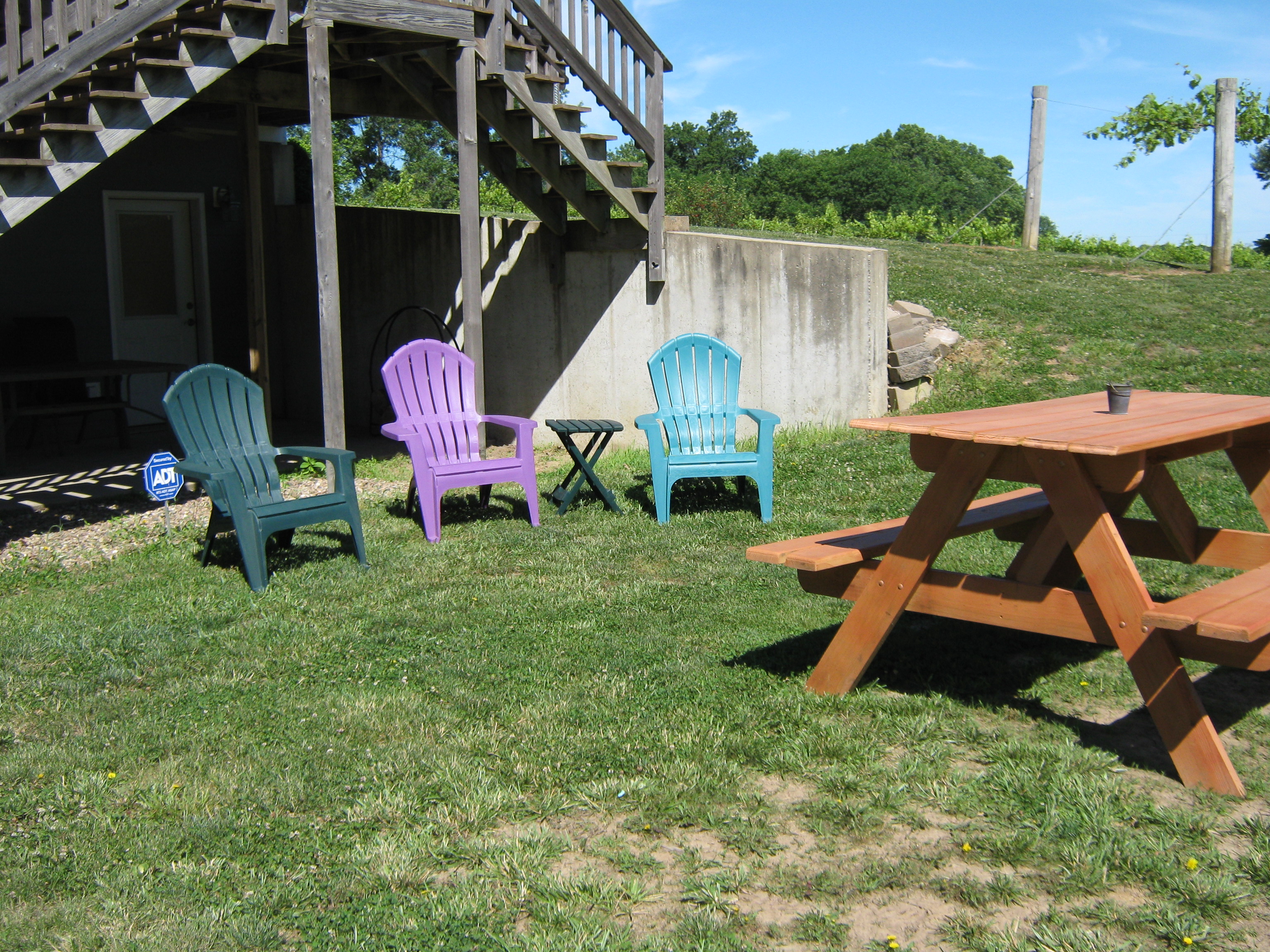 Hummingbird Vineyard and Winery- Outdoor seating. One picnic table and three colorful plastic lawn chairs.