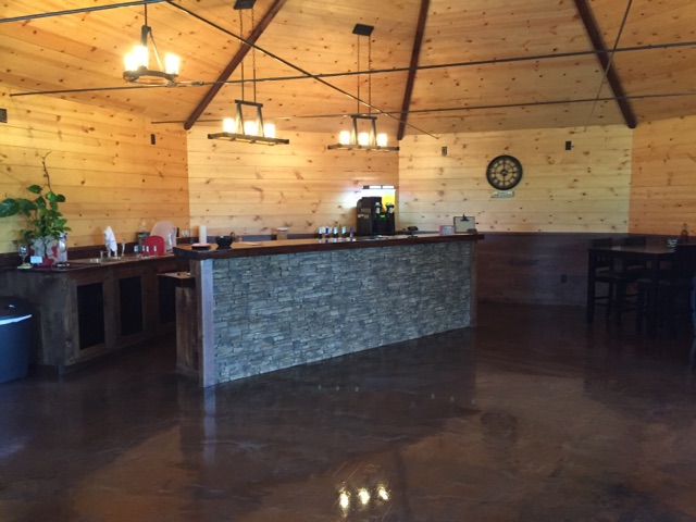 Backyard Vine & Wine, LLC - indoor photo of a large room with a high ceiling, a bar made of stone and a hardwood floor.