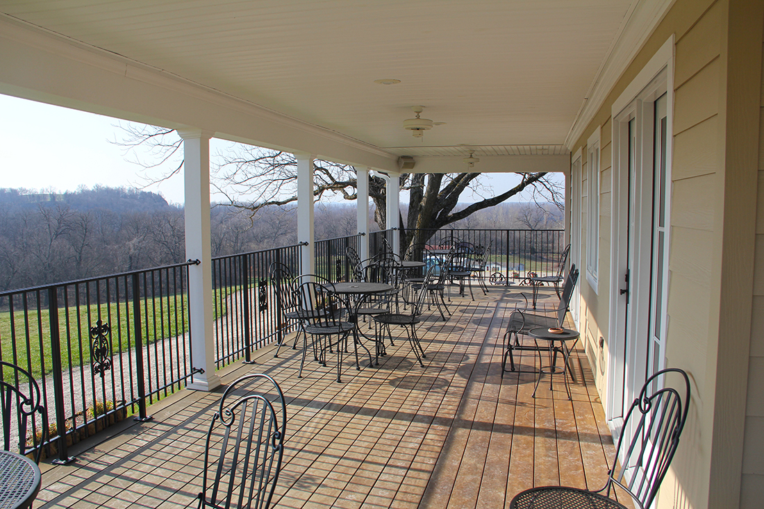 Lost Creek Vineyard - outdoor photo, daytime, of a large porch with wooden floors. Various patio furniture is on the porch, which overlooks a large green field.