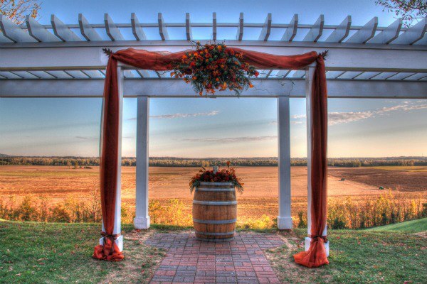 Mount Pleasant Estates- A wedding arch set up with a wooden barrel in the middle, overlooking a field.