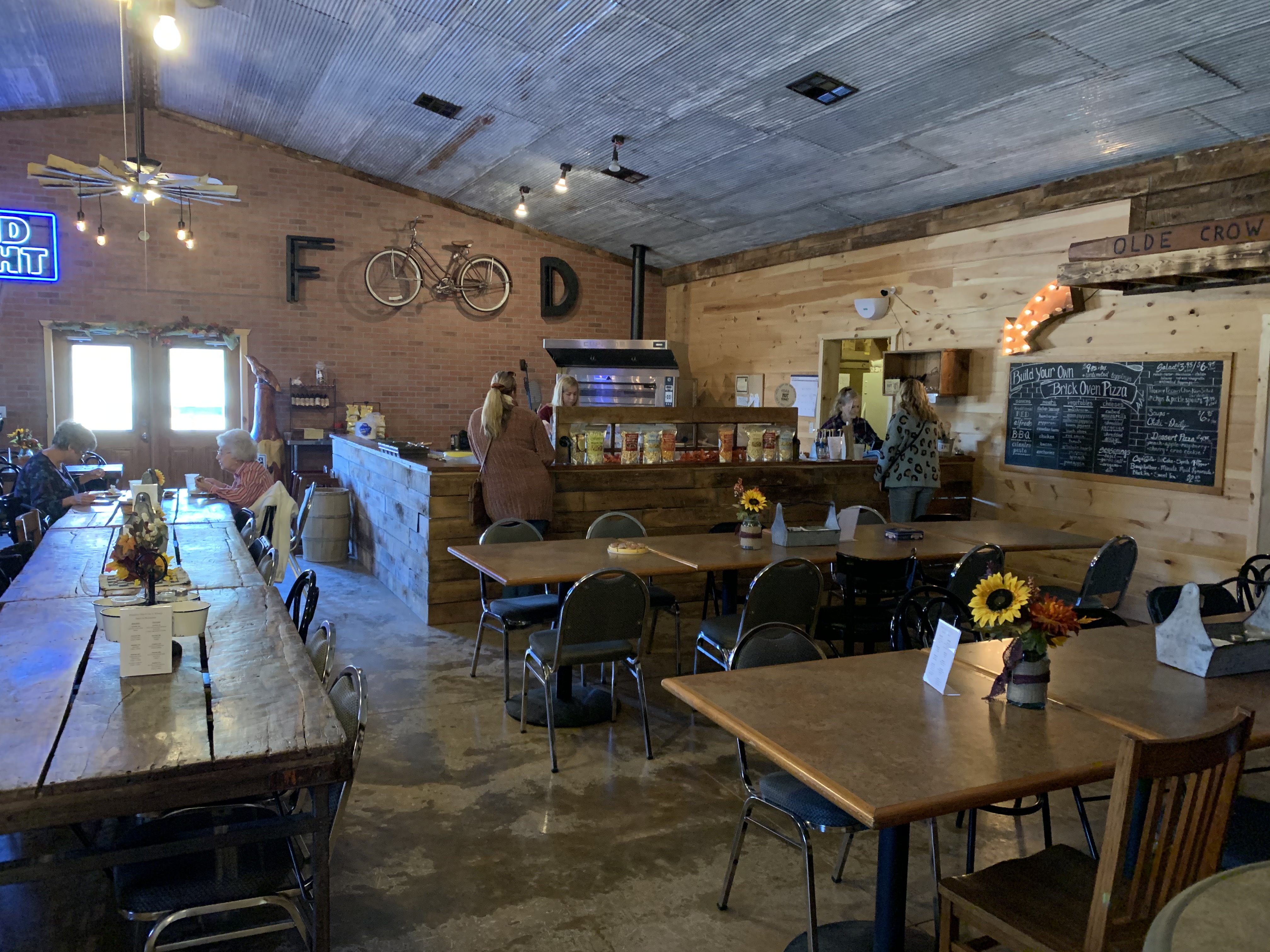 Primitive Olde Crow and Winery- Indoor food and pizza area with several tables with sunflowers.