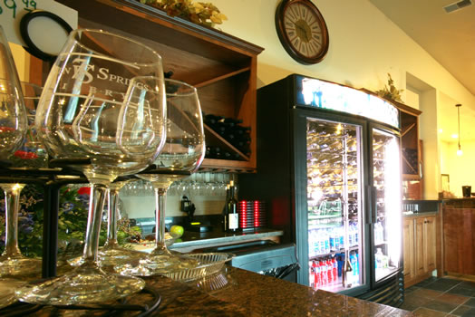 Seven Springs Winery - indoor photo of a bar with wine glasses in the foreground and a beverage cooler in the background.