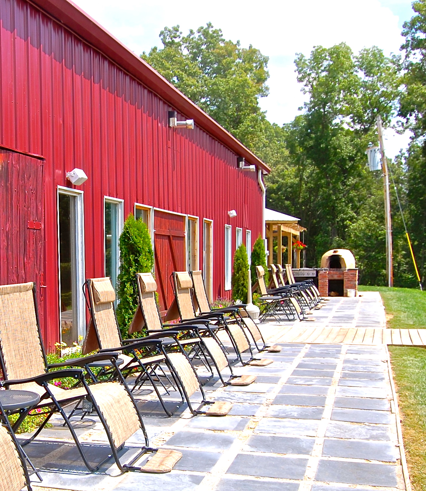 Shawnee Bluff Vineyard - outdoor photo, daytime, of a large stone patio area in front of a large red building. Chairs line the patio.