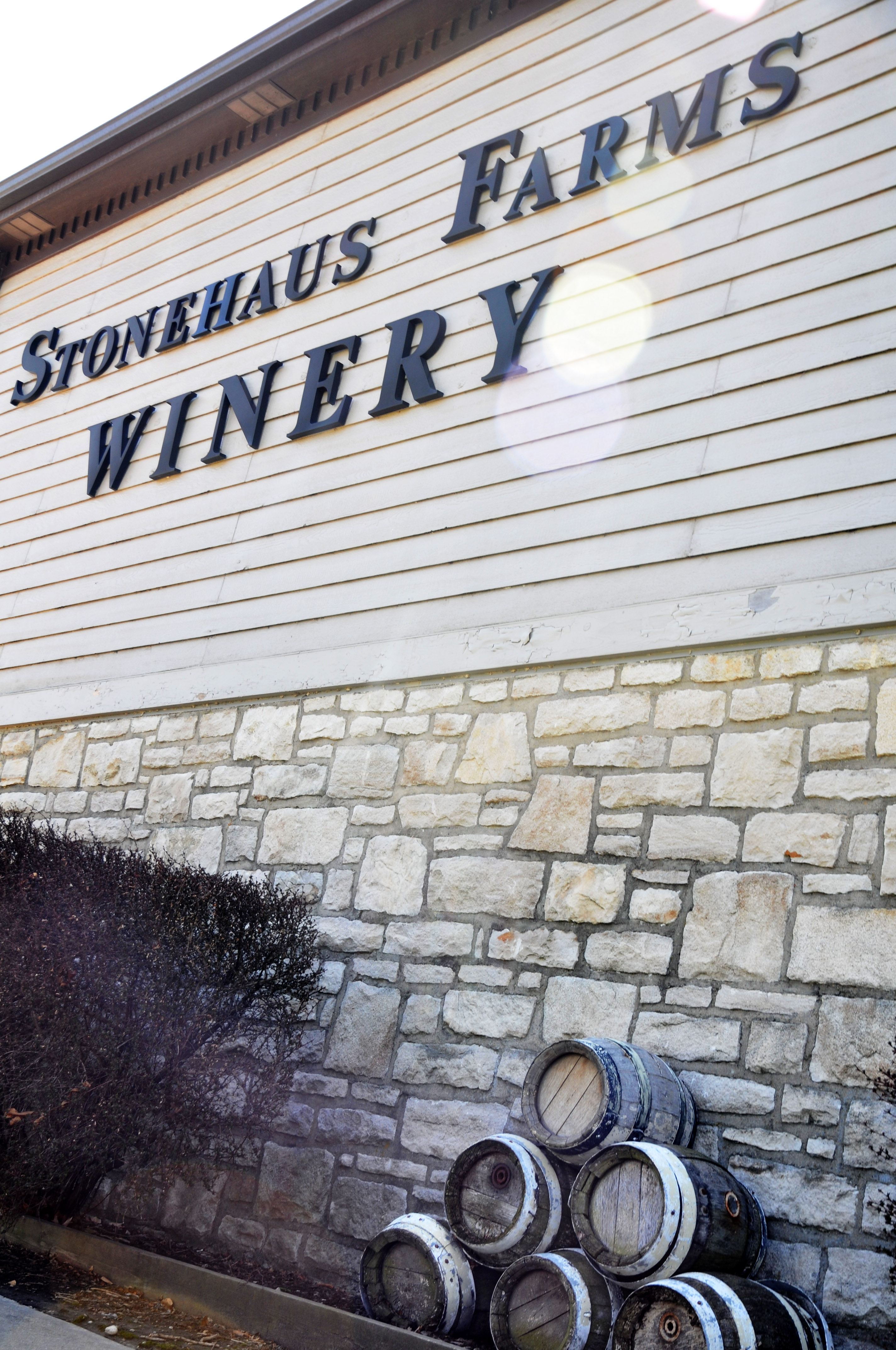 Stonehaus Farms Vineyard & Winery - outdoor photo, of a large building of stone and siding, with the winery's logo on the side. Wine barrels are in the foreground.