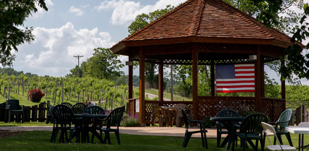 Outdoor photo, daytime, of a large wooden gazebo surrounded by patio furniture.