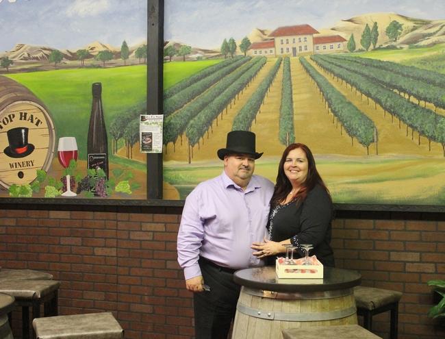 Top Hat Winery - indoor photo of two people in front of a large mural inside a building. The man is wearing a top hat.