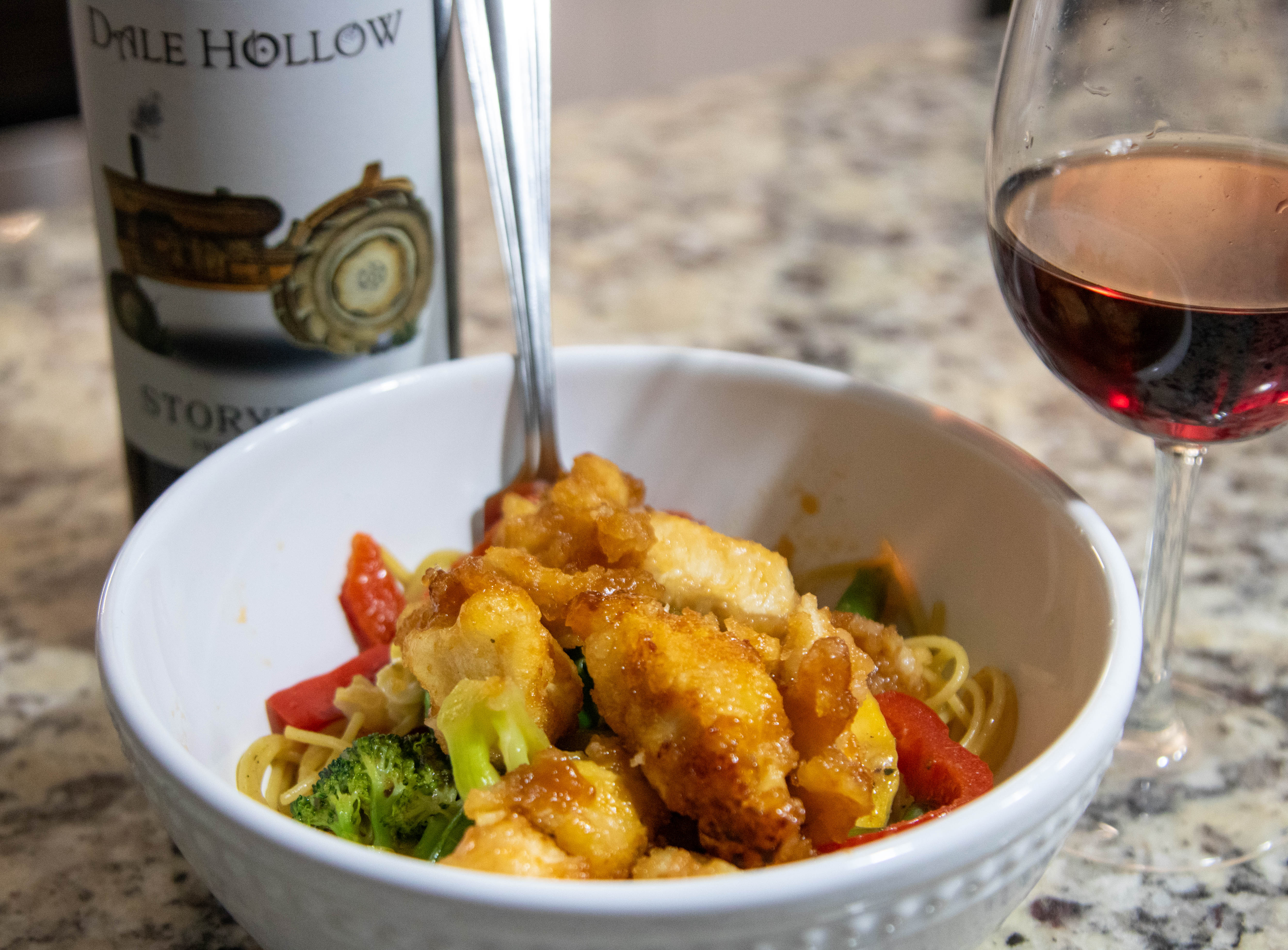 Sweet and sour chicken in a bowl with a glass of concord wine next to it