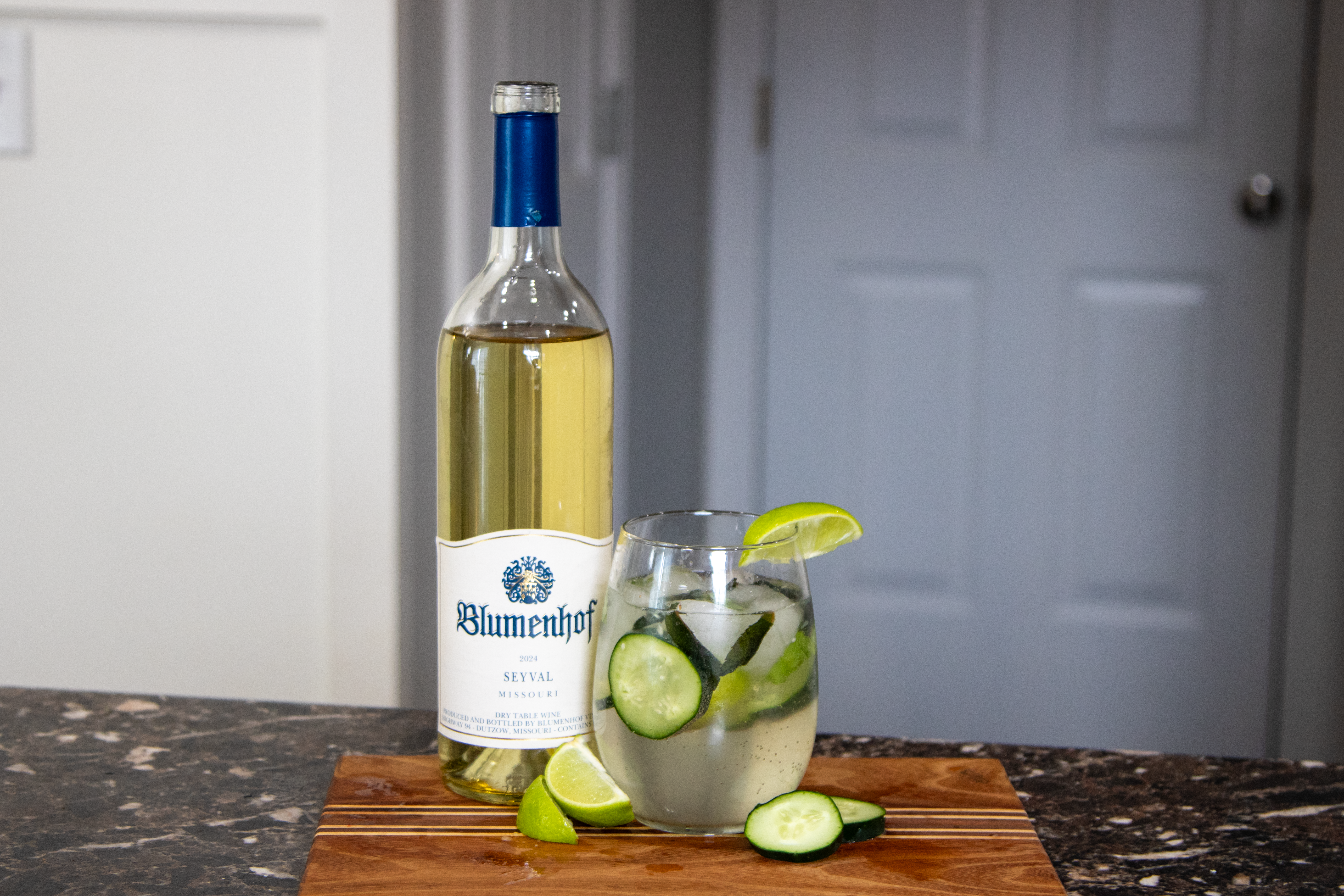 Finished Cucumber herb Spritzer next to wine bottle, lime and cucumber
