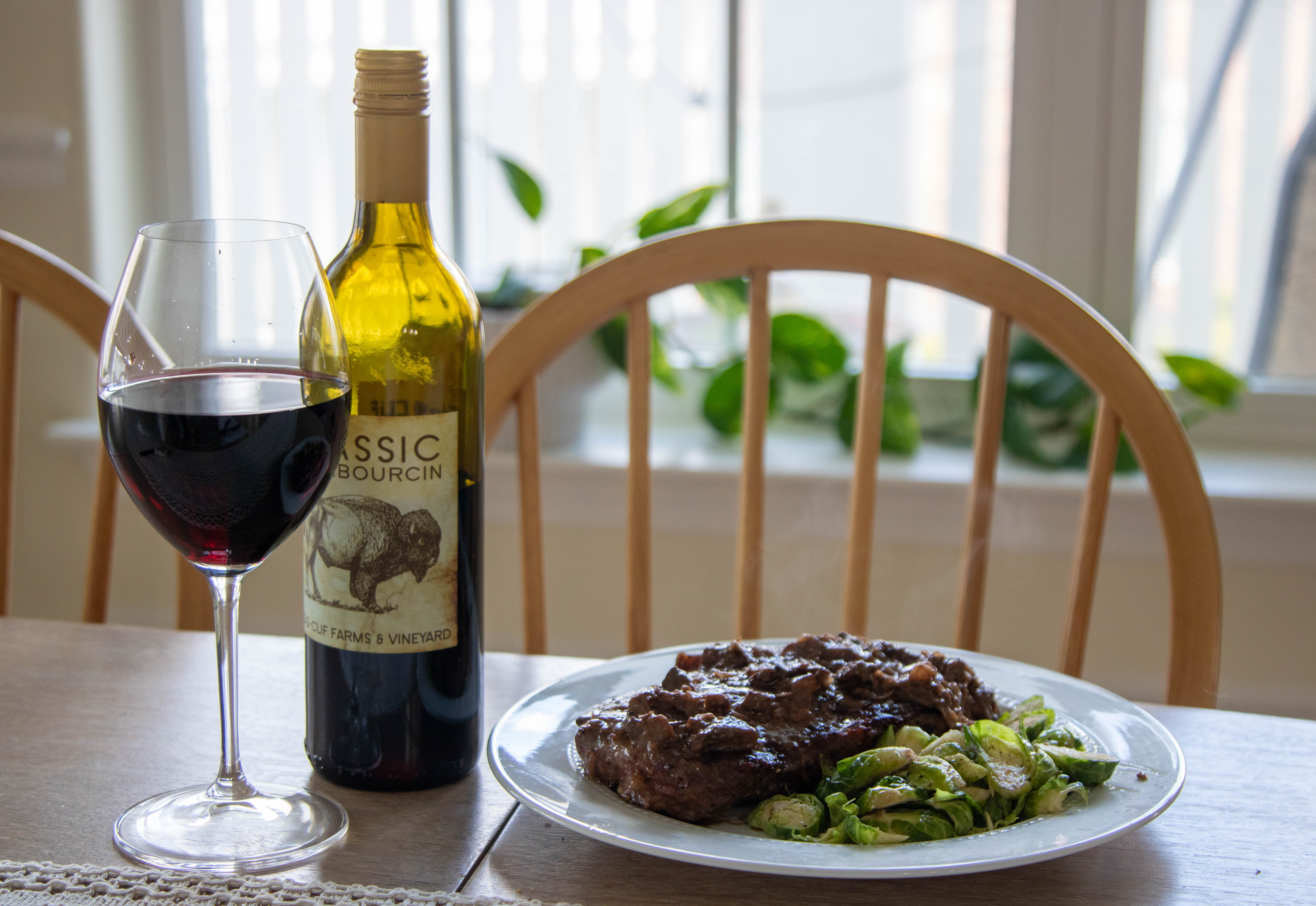 Plated meal of steak and brussel sprouts with a glass of wine sitting next to it
