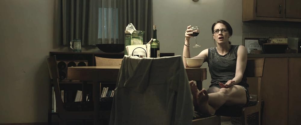 Girl sitting at a table in a dining room holding a glass of wine with her feet propped up