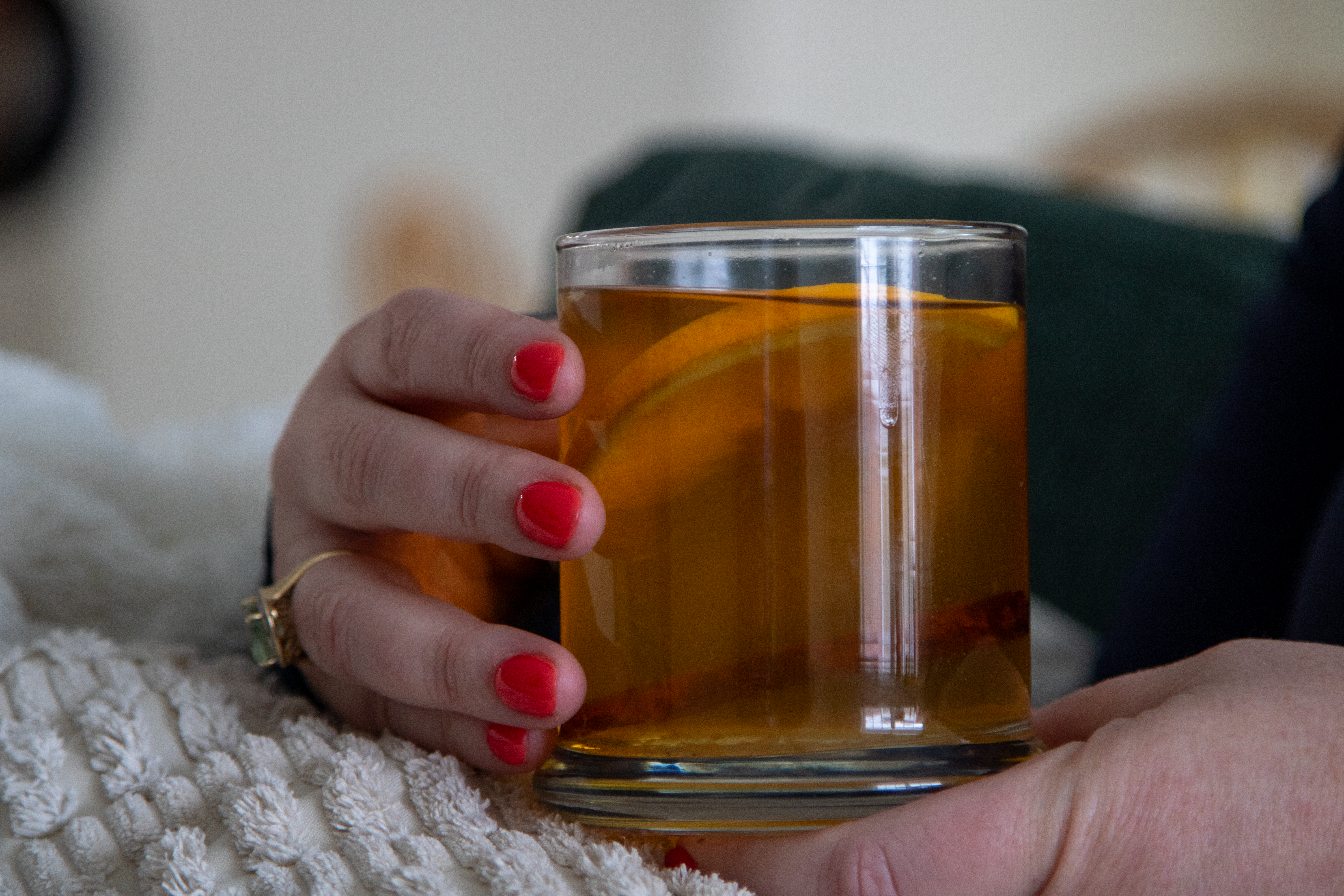 Finished clear glass of mulled wine held by woman on couch with blanket.