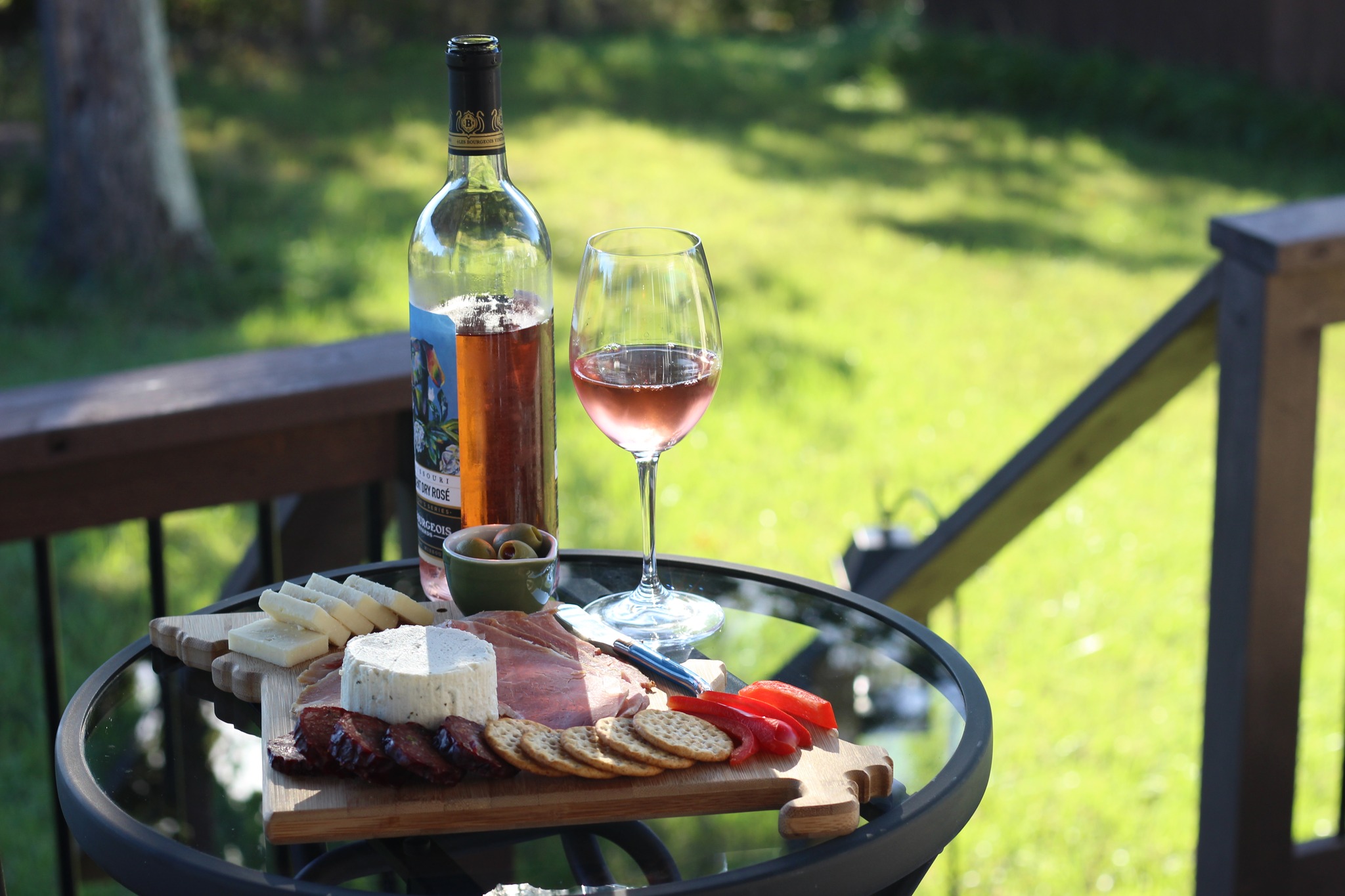 A glass of rosé sitting outside on a table with a meat and cheese platter