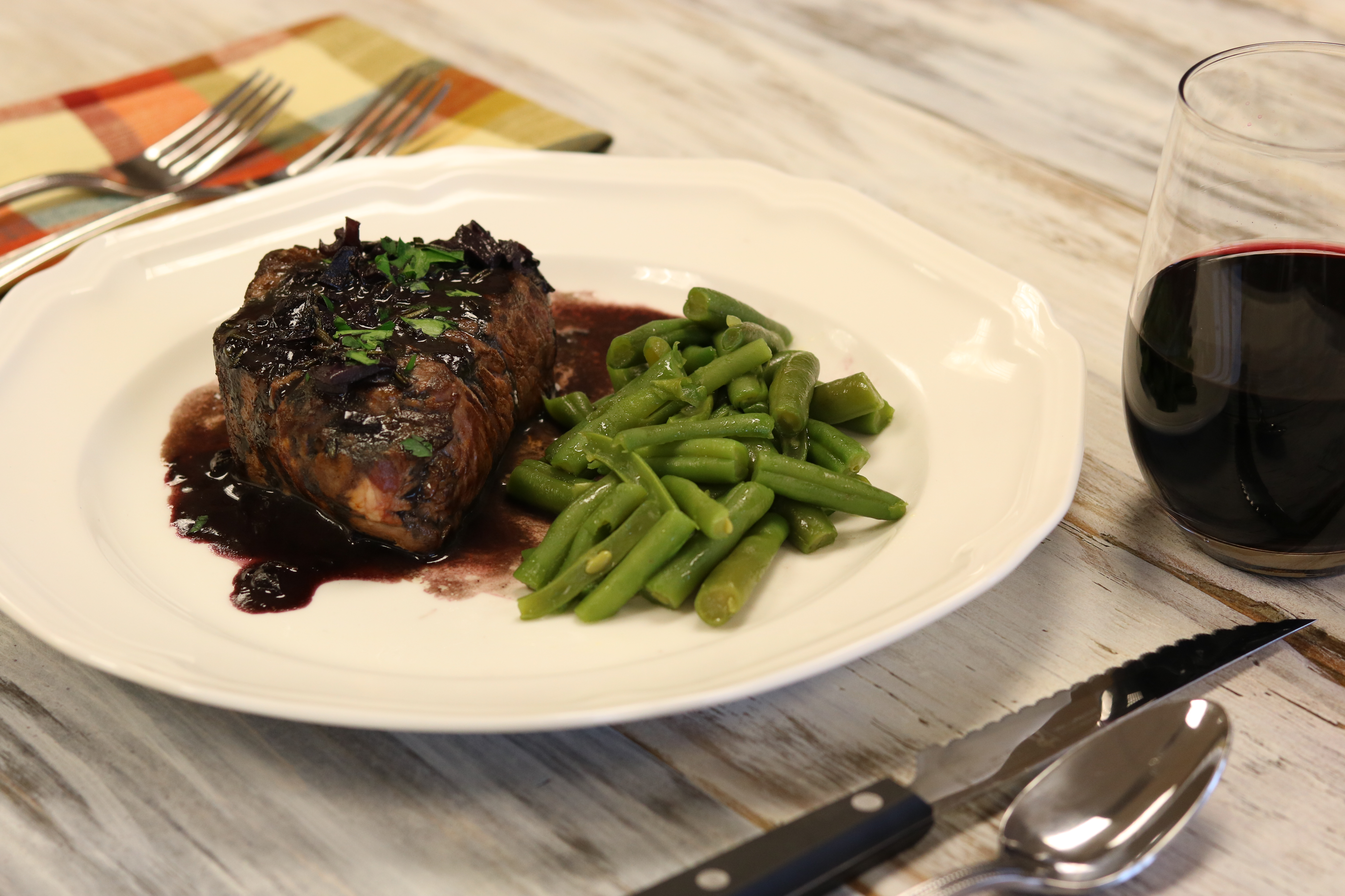 Plate with steak and green beans on it with silverware and a glass of wine.