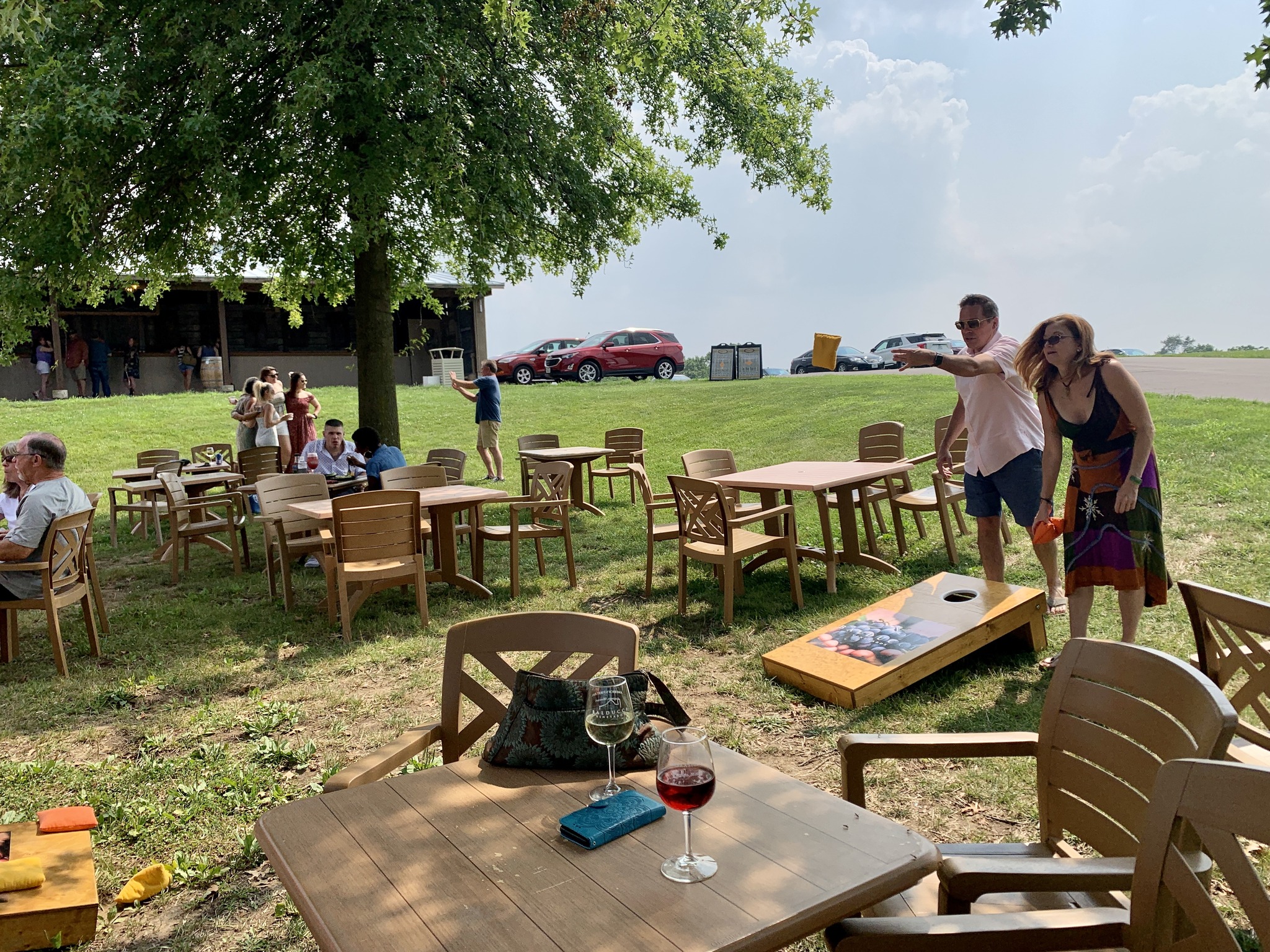 Photo of a family playing cornhole with wine glasses sitting on a picnic table.