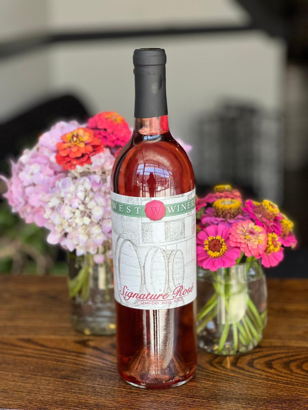A rose bottle with flowers sitting on a counter top. 